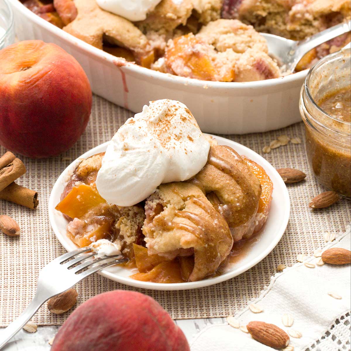 A plate of gluten-free peach cobbler with oat and almond flour and whipped cream on top.