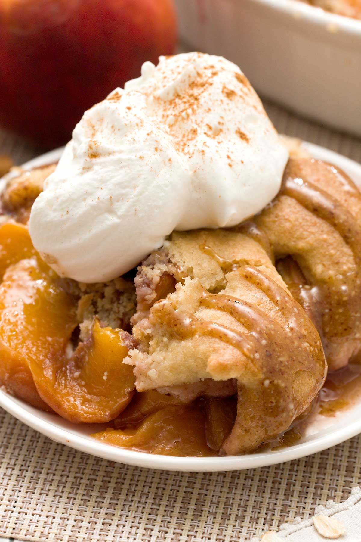 A close-up of gluten-free peach cobbler with oat and almond flour and whipped cream on top.