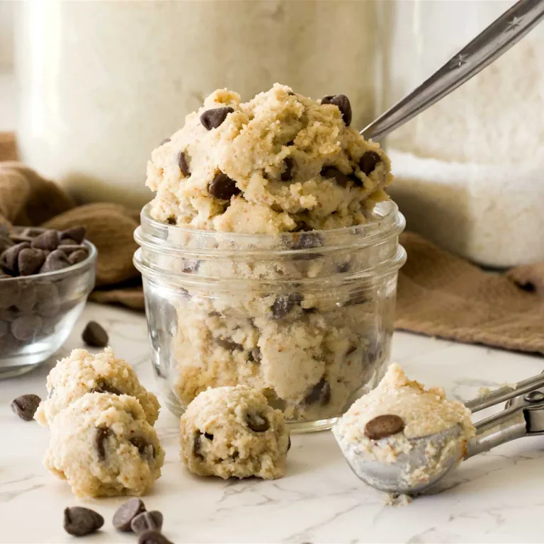 A small mason jar full of edible chocolate chip cottage cheese cookie dough with chocolate chips and a cookie scoop.