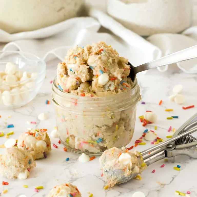 A small mason jar full of edible funfetti cottage cheese cookie dough with white chocolate chips with a cookie scoop.