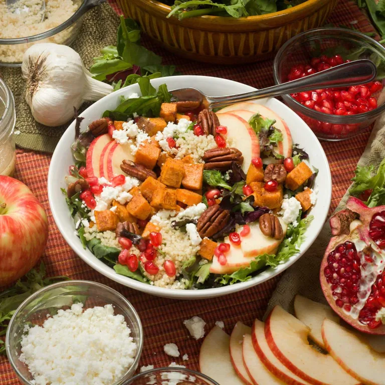 Fall harvest salad with sweet potatoes, apples, pomegranate seeds, and pecans in a white bowl.