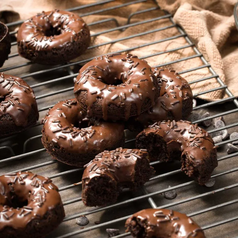 Stack of gluten-free chocolate glazed donuts with chocolate sprinkles on a cooling rack.
