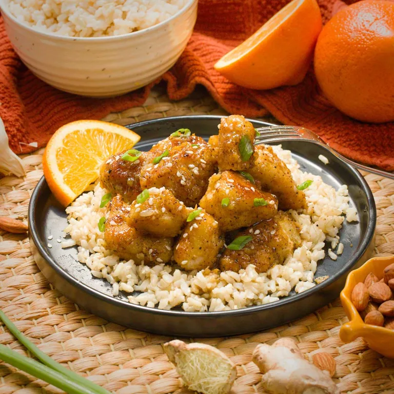 Gluten-free orange chicken on a bed of brown rice with a slice of orange.