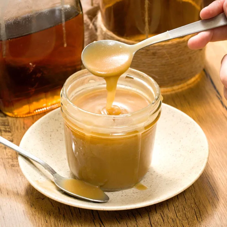 Homemade maple syrup salted caramel sauce in a small jar dripping off a spoon.