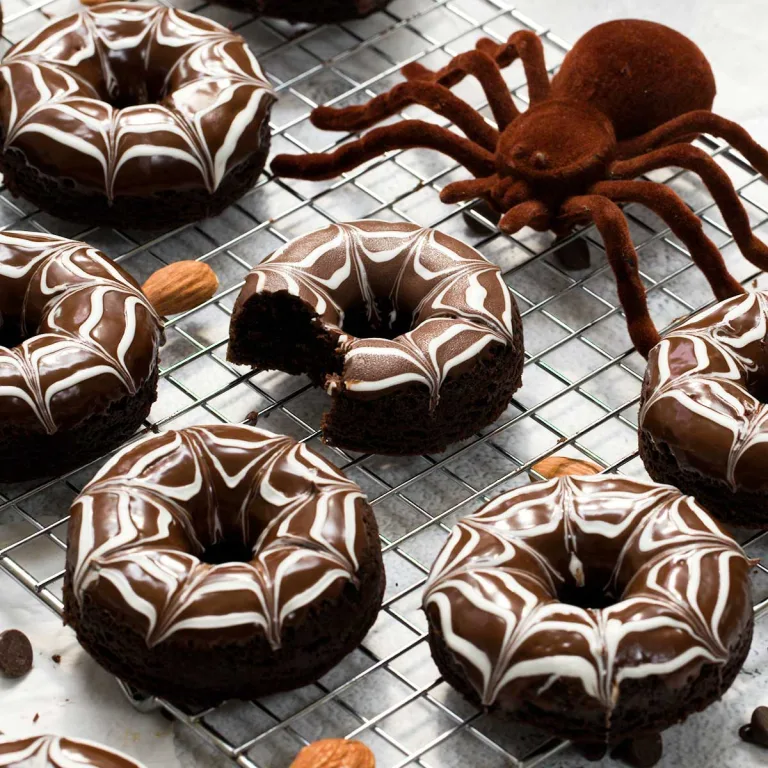 Gluten-free Halloween spiderweb chocolate donuts on a cooling rack with a large spider.