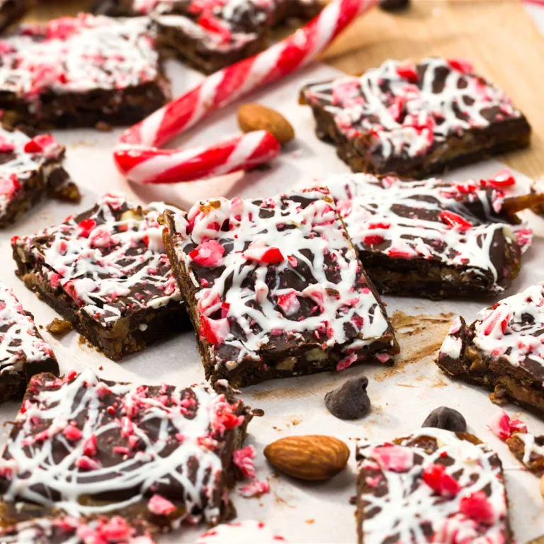Squares of peppermint chocolate egg bark spread out on parchment paper next to a candy cane.