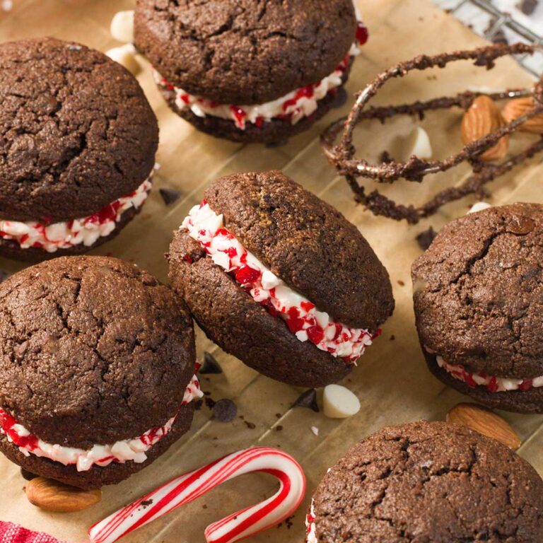 Several chocolate peppermint whoopie pies on parchment paper next to candy canes.