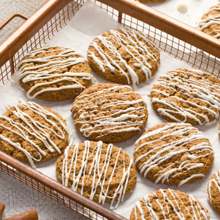 A copper wire tray with gluten-free iced molasses cookies on a parchment paper.
