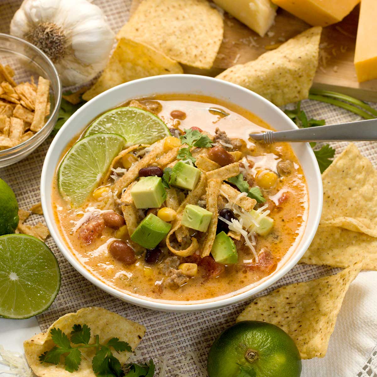 A bowl of Panera beef tortilla soup in a white bowl with avocado and sliced lime wedges on top.