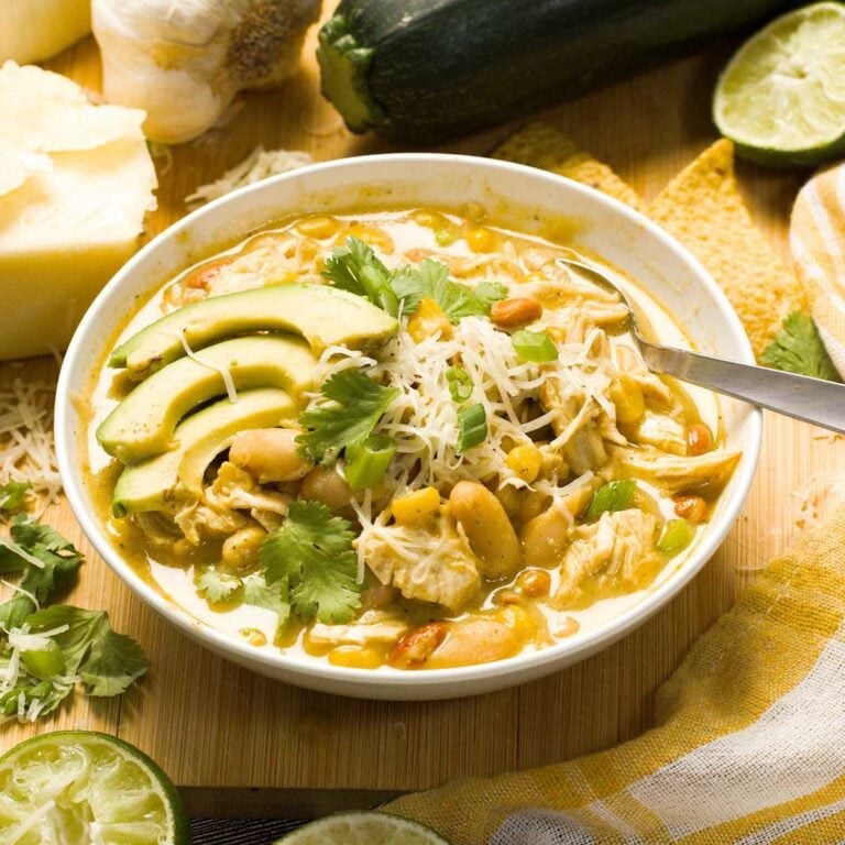 A bowl of Cheesecake Factory copycat white chicken chili in a white bowl with wedges of avocado on top.