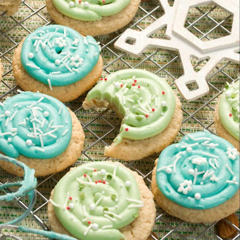 Blue and green frosted sugar cookies with sprinkles and a bite taken out of a green cookie.