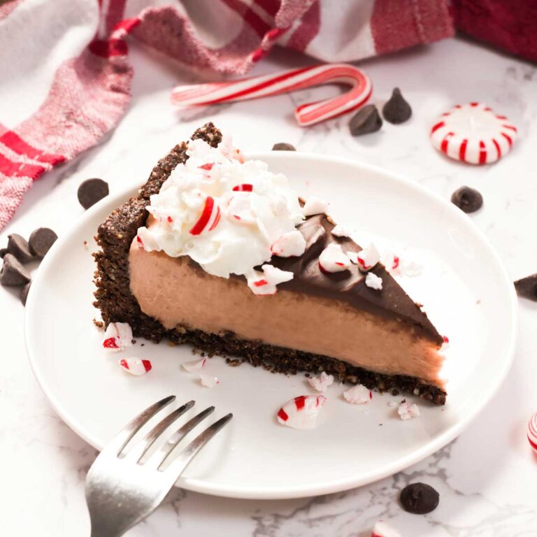 A slice of no-bake peppermint cheesecake on a white plate with peppermint candy pieces on top.