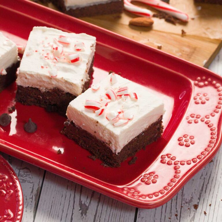 Two gluten-free black bean peppermint brownies on a red plate with crushed candy canes on top.
