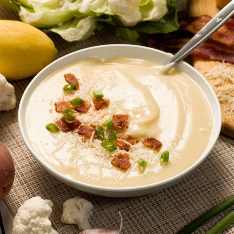 A bowl of cauliflower zucchini soup with bacon, cheese, and green onion.