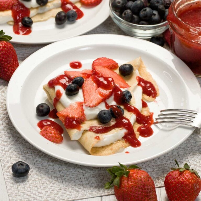 Cottage cheese filled crepes with strawberries and blueberries on a plate.