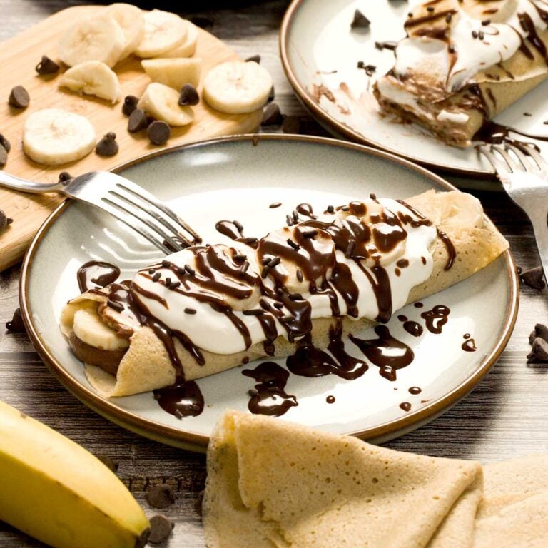 Chocolate banana filled crepe covered in chocolate sauce on a plate.