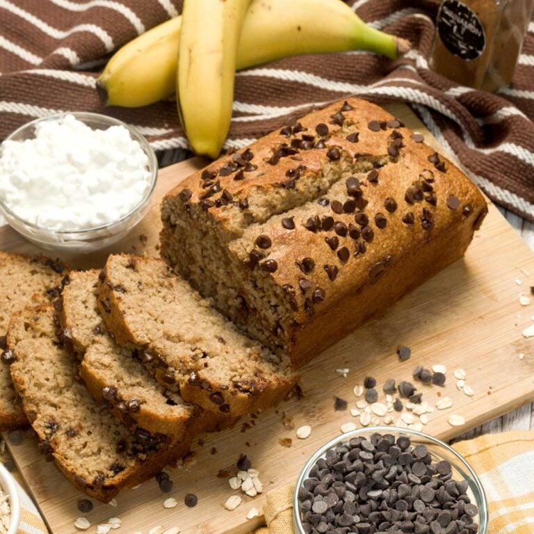 A loaf of gluten-free cottage cheese banana bread with chocolate chips on a cutting board.