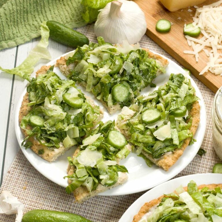 A caesar salad chicken crust pizza on a white plate.