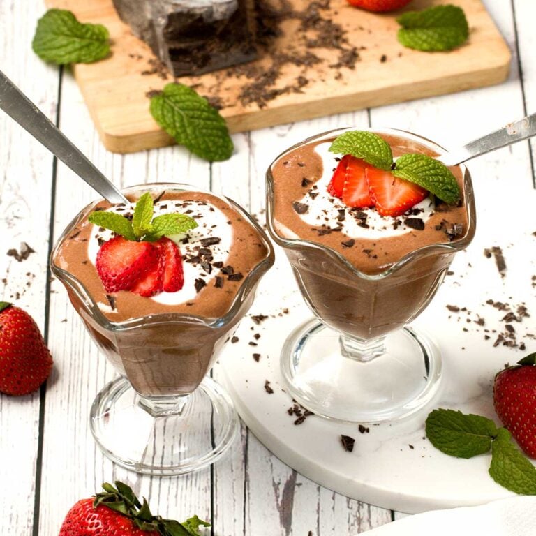 Two glass bowls of chocolate protein mousse with cream, strawberries and chocolate.