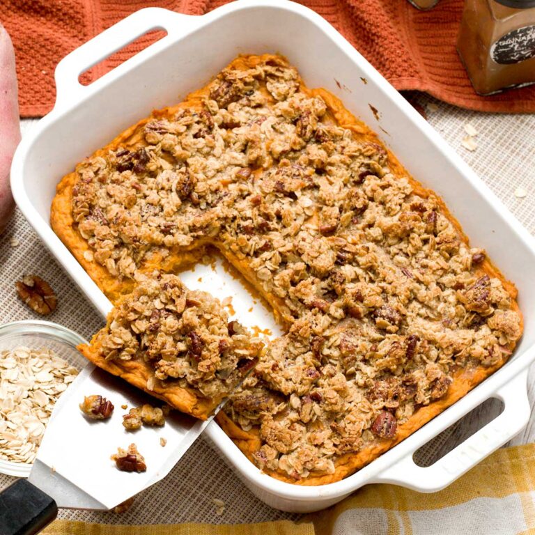 A spatula with a portion of sweet potato casserole being lifted out of a baking dish.