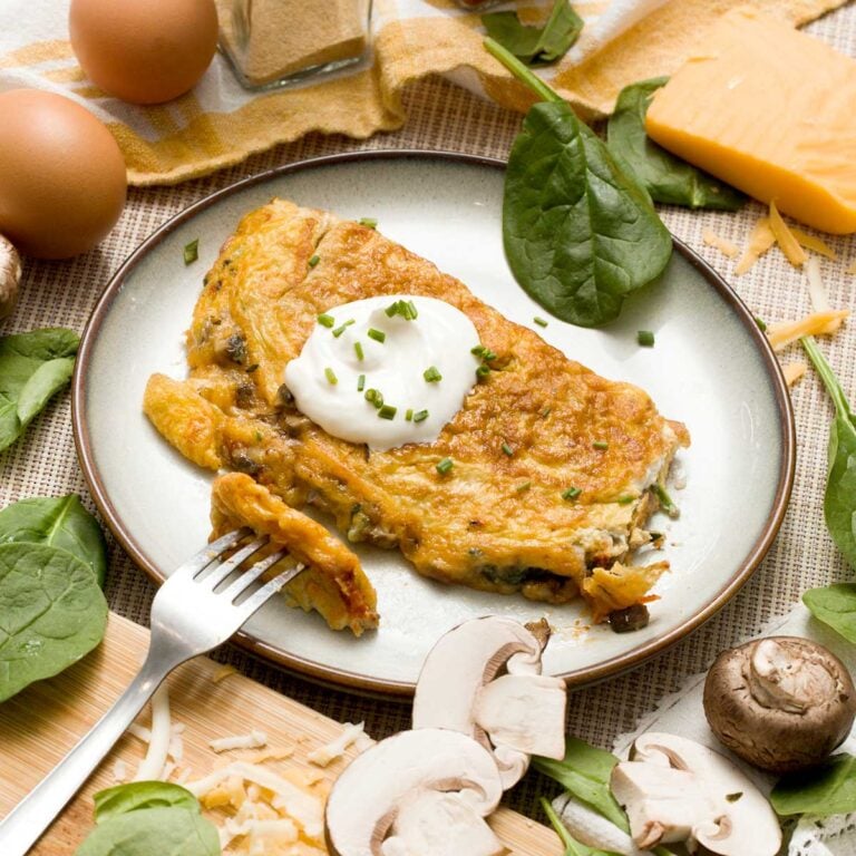 A mushroom spinach omelet on a plate with a bite on a fork next to it.