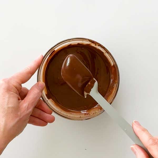 The melted chocolate on a spatula in a bowl.