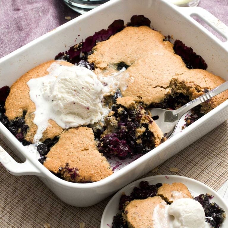 A baking dish with gluten-free blueberry cobbler with oat flour next to a plate with ice cream on top.