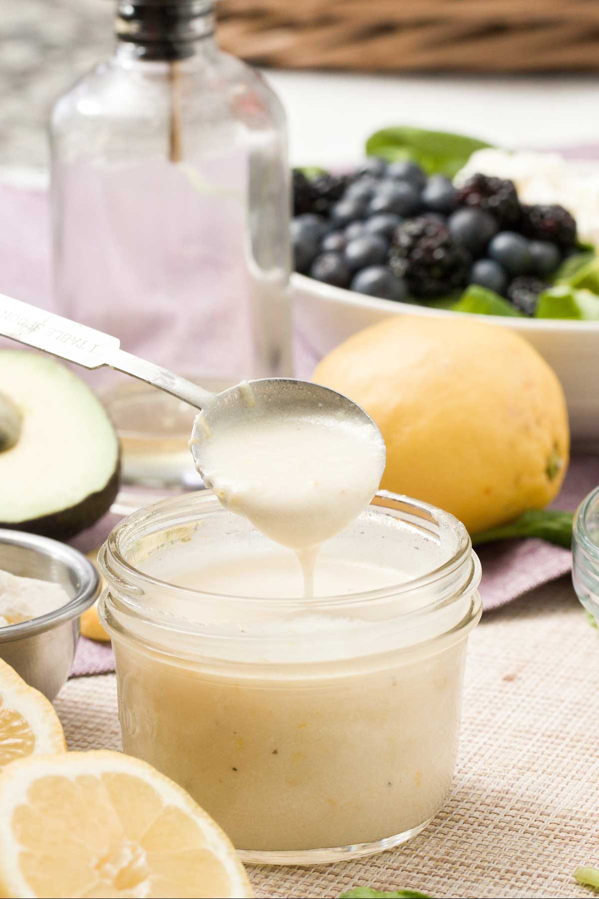 A jar of honey lemon vinaigrette with greek yogurt in a spoon.