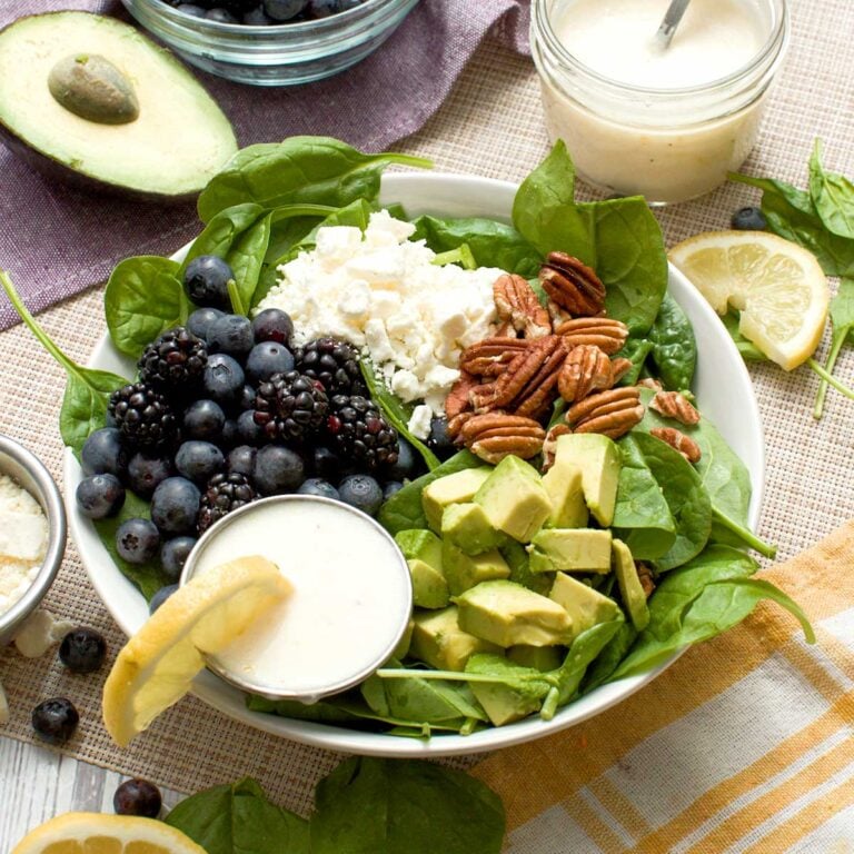 Spinach blueberry salad with feta, avocado & creamy honey lemon dressing in a bowl.