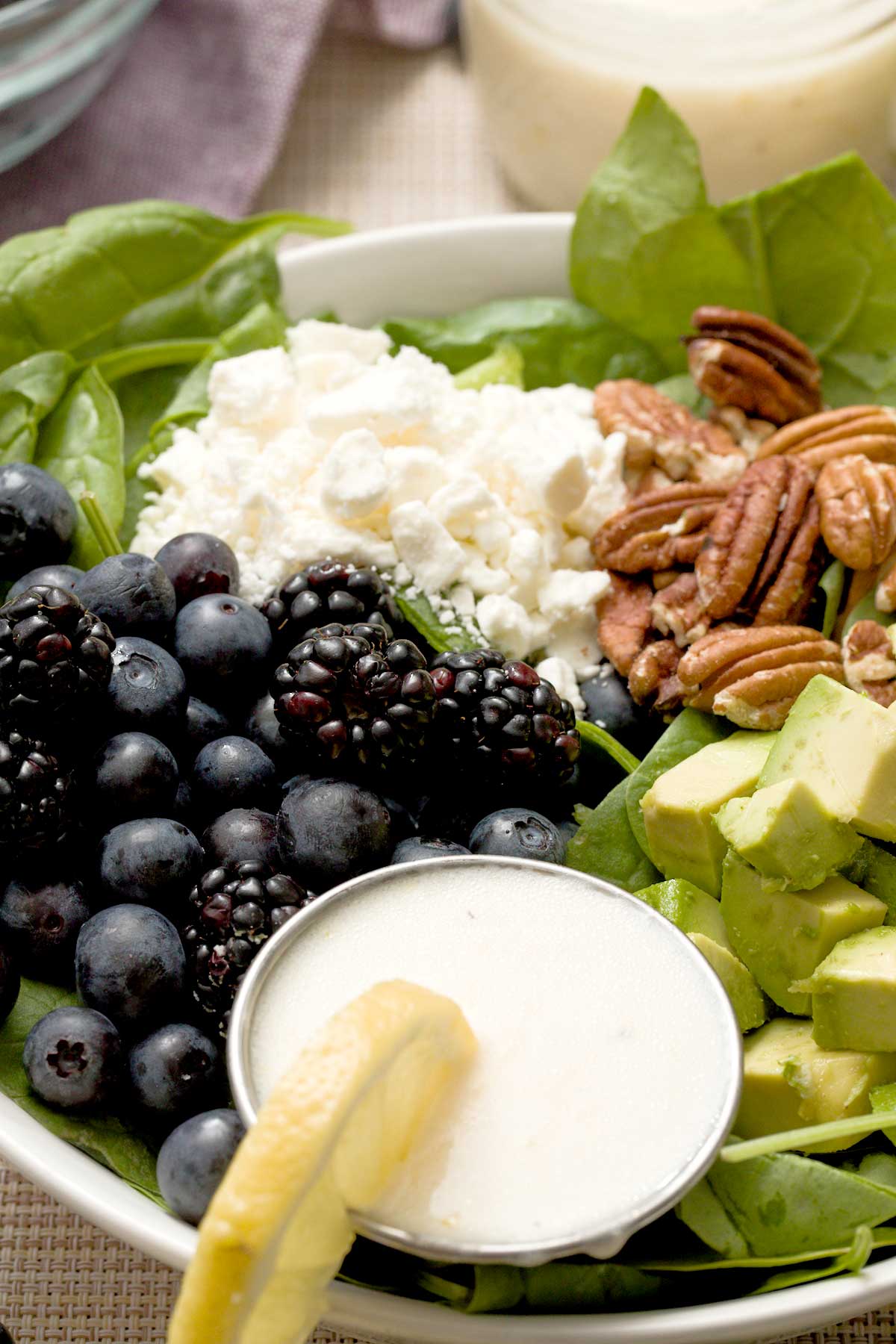 Close-up of Spinach blueberry salad with feta, avocado & creamy honey lemon dressing in a bowl.