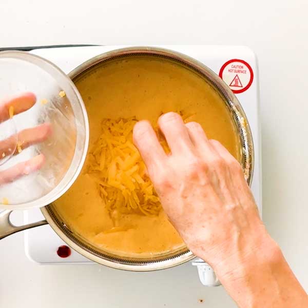 Adding graded cheddar cheese to the thickened pasta sauce in the sauce pan.