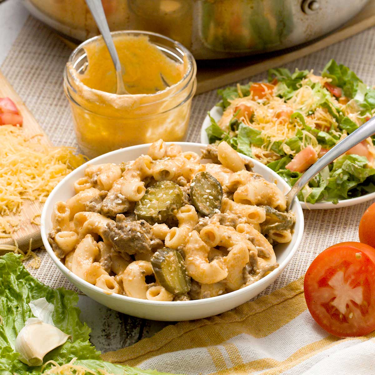 A bowl of high protein big Mac pasta next to a plate with a green salad with big Mac sauce dressing.