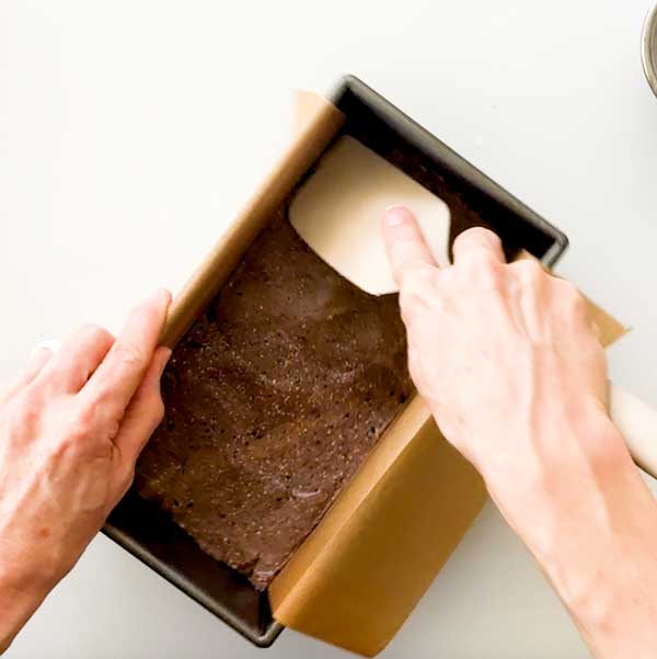 Pressing the protein bar dough into a bread pan lined with parchment paper.