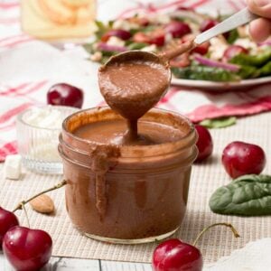A spoon full of cherry balsamic vinaigrette with fresh cherries.