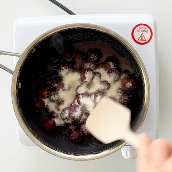 Stirring sugar in with the cherries in the saucepan.