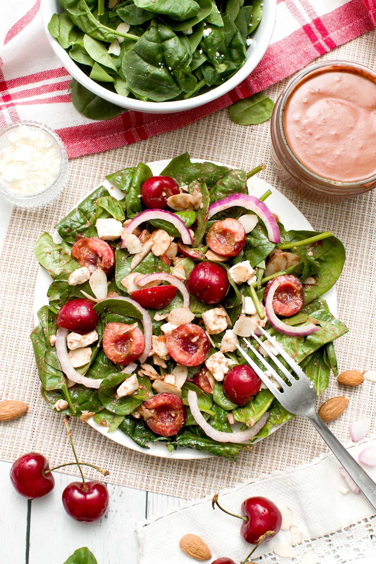 The top view of a cherry spinach salad with feta cheese, almonds and red onion and a cherry balsamic vinaigrette.