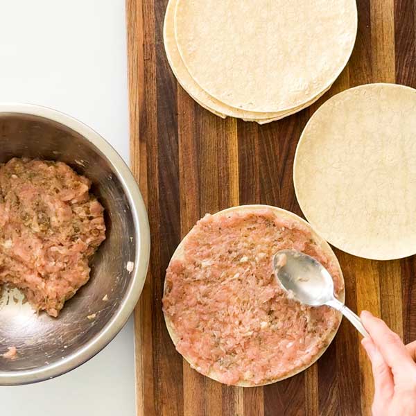 Spreading ground chicken mixture on a jumbo corn tortilla.