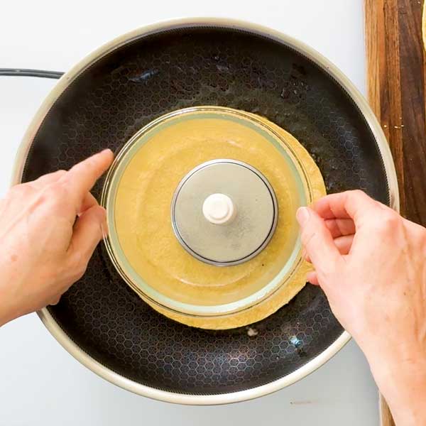 Placing a glass bowl on top of the chicken smashed taco in the skillet.