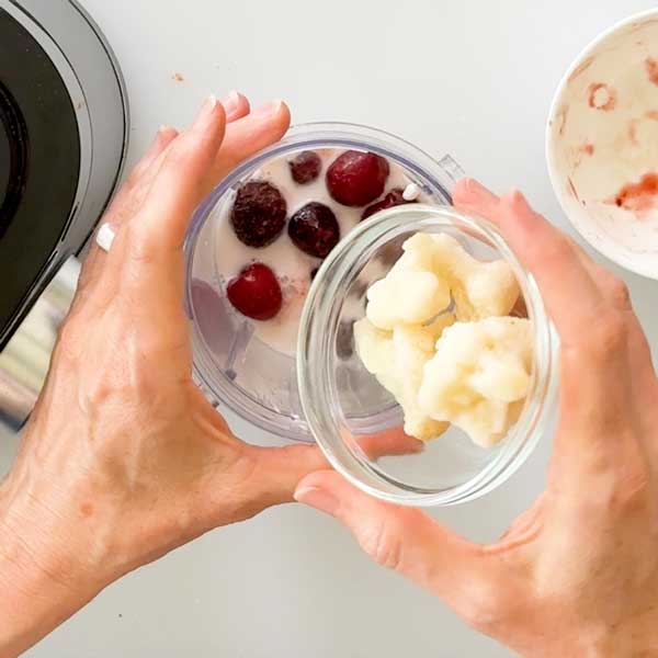 Adding the frozen cherries and cauliflower to the blender cup.