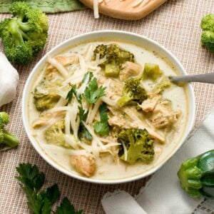 A bowl of creamy zucchini broccoli chicken soup with Greek yogurt and shredded cheese and parsley on top.