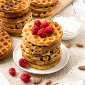 A stack of cottage cheese protein waffles with almond flour on a plate with raspberries.