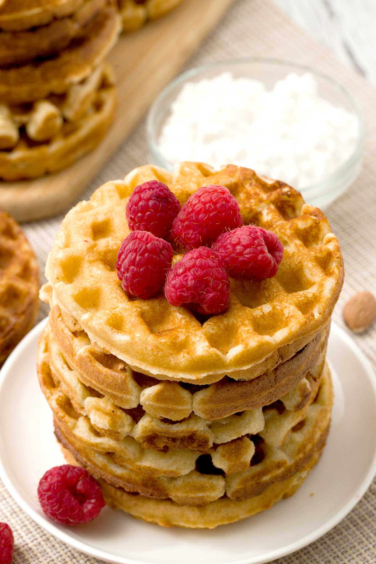 A close-up of a stack of cottage cheese waffles with almond flour on a plate with raspberries.