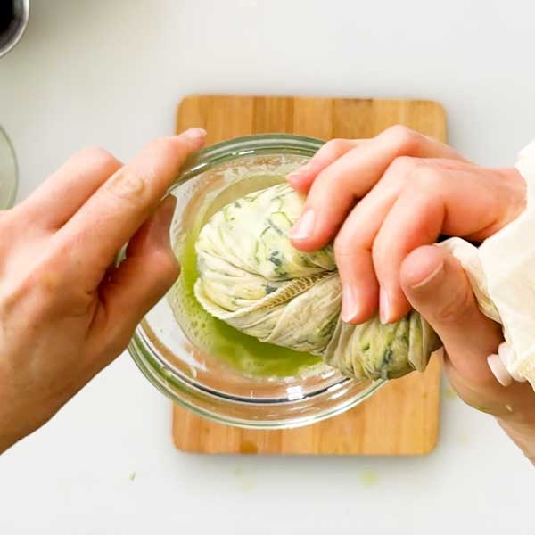 Squeezing the liquid out of the shredded zucchini in a strainer bag.