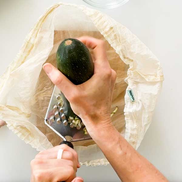 Shredding a zucchini into a strainer bag.