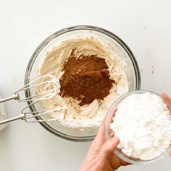 Adding the powdered sugar to the frosting mixture.