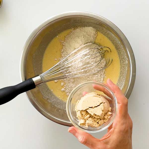 Adding the dry ingredients to the pancake batter in a mixing bowl.