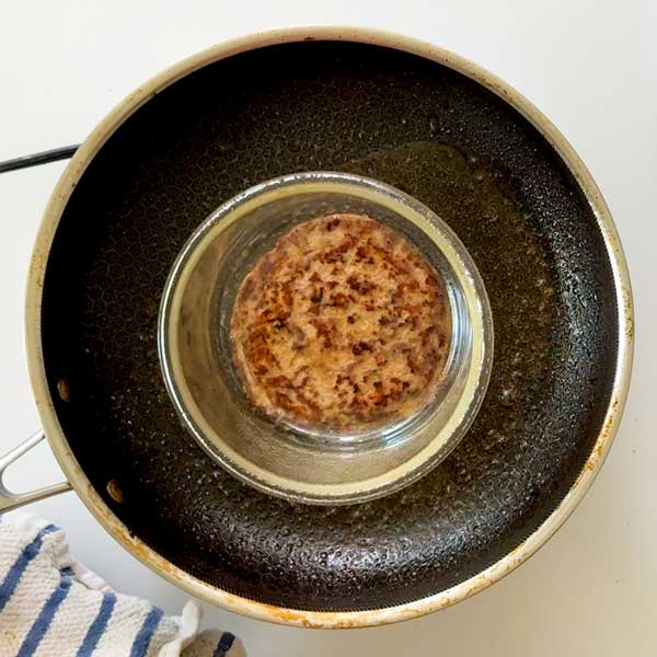 Placing the flat Glass dish on top of the turkey patty after flipping it over in the skillet.