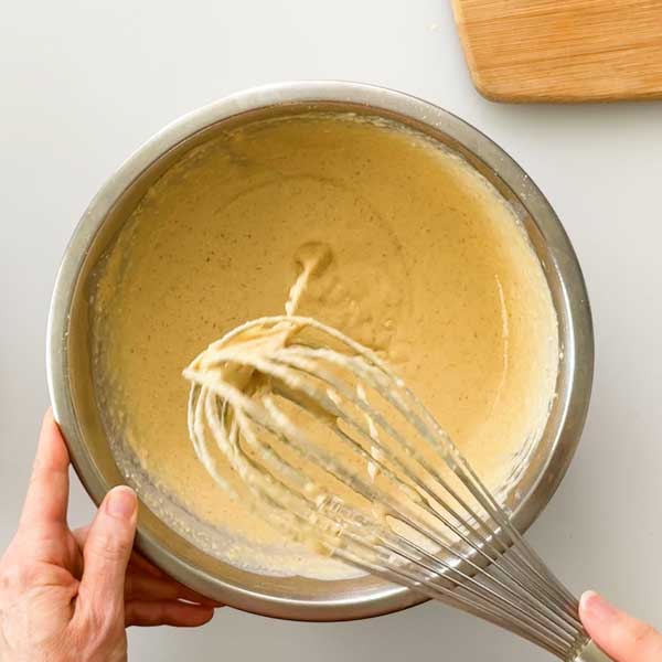 Mixing the wet ingredients into the pancake batter for a smooth consistency.