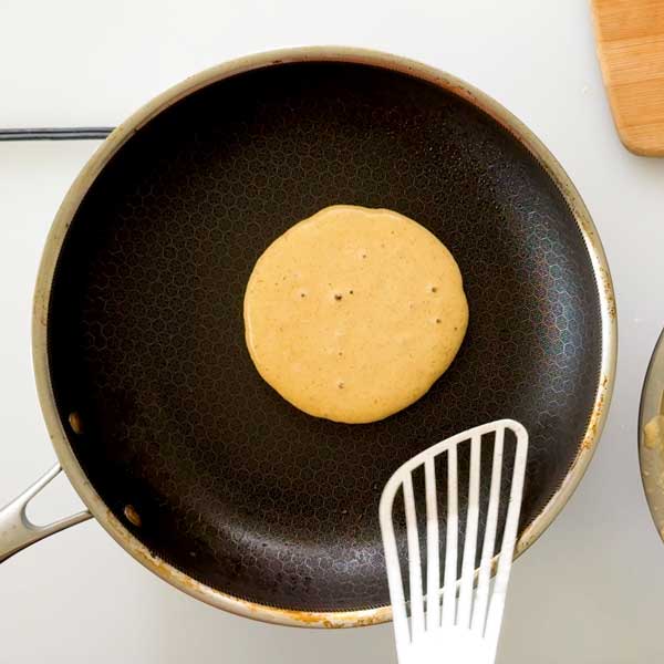 Waiting for bubbles to form on the top of the pancake before flipping it in the skillet.