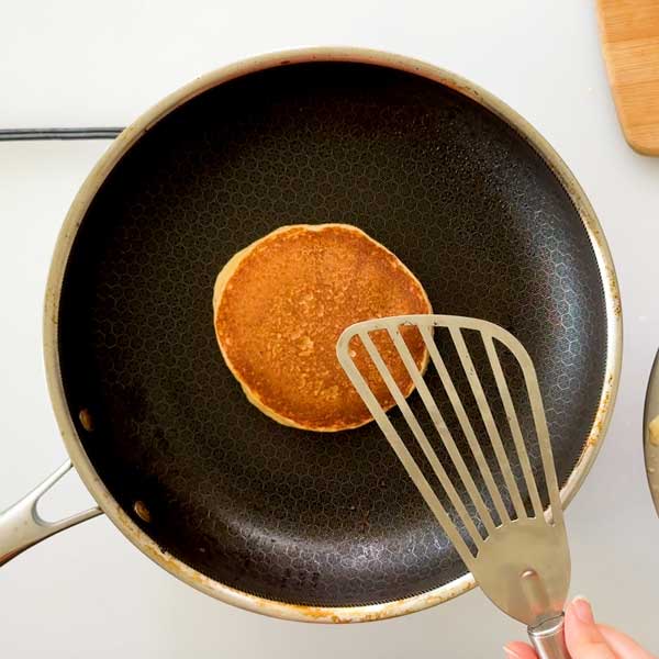 Flipping the toasted pancake in a skillet with a spatula.